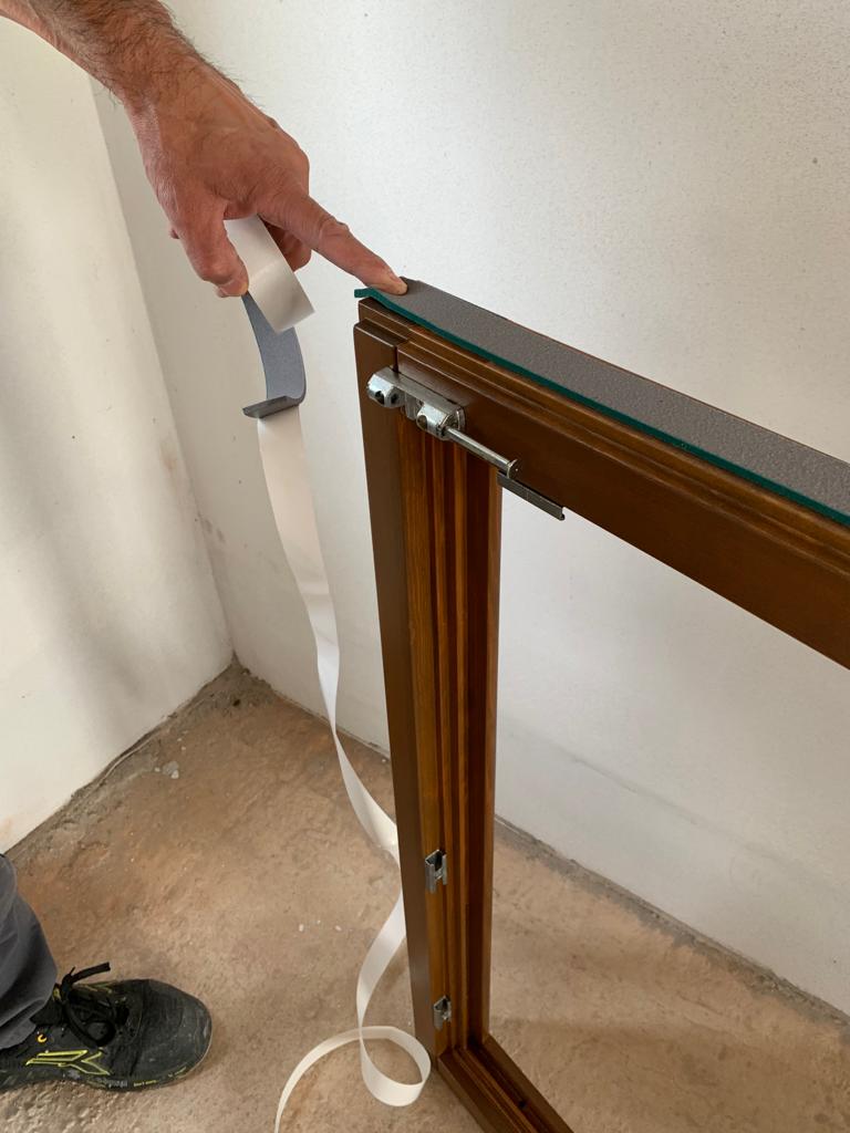 Installatore applica il nastro sigillante e barriera vapore sul profilo esterno del serramento in legno.